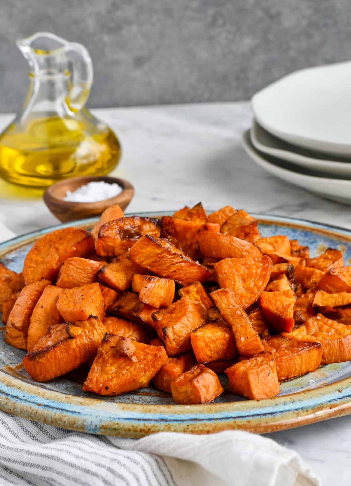 Easy Roasted Sweet Potatoes piled on a plate with olive oil and salt in background