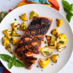 A healthy fish dinner of blackened salmon served on a white dinner plate, surrounded by yellow grilled vegetables.