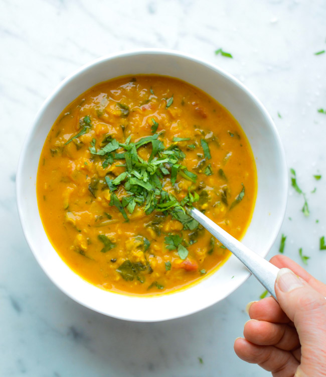 Golden Red Lentil and Kale Soup (Vegan) in bowl with hand