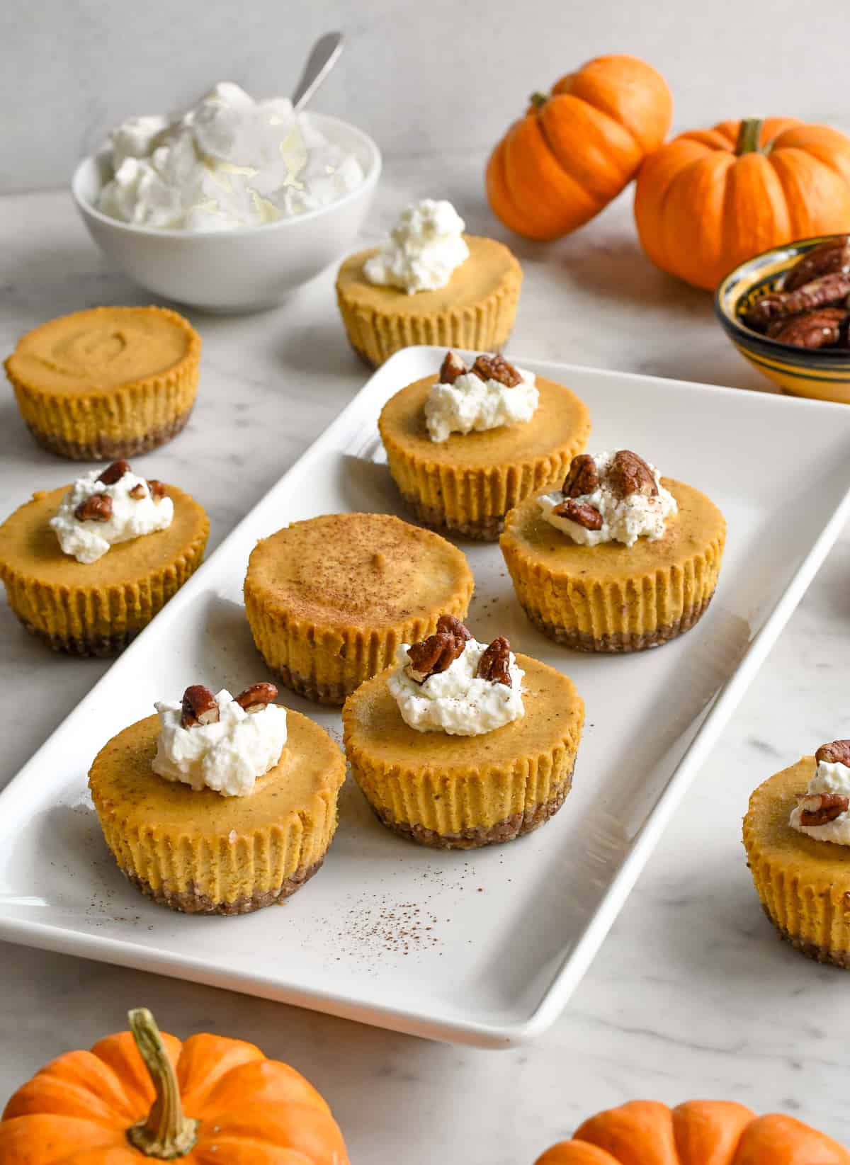 Vegan Mini Pumpkin Cheesecakes on platter with whipped cream and peacans