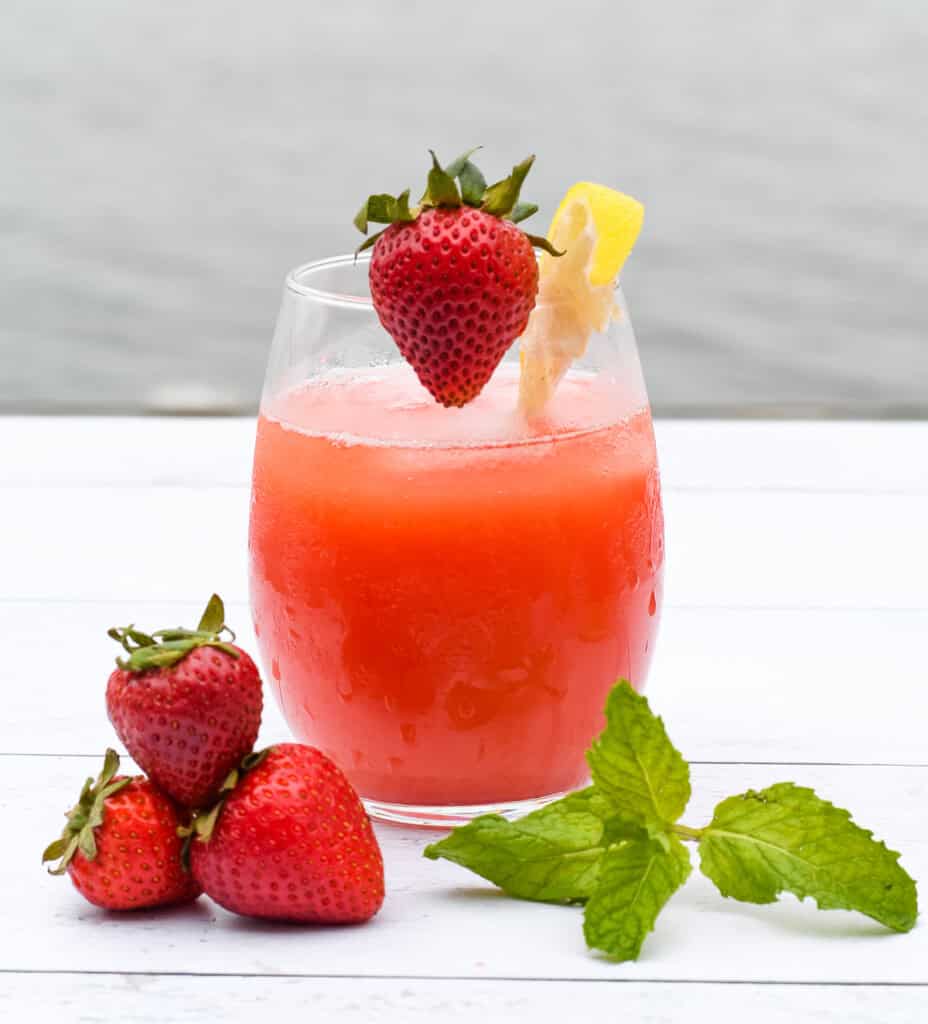 Homemade Strawberry Lemonade close up with a pile of strawberries and a sprig of mint 