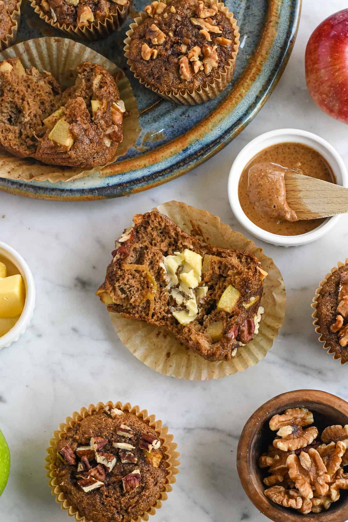 Healthy Apple Muffins overview on plate with almond butter in a ramekin and a muffin broken open spread with butter