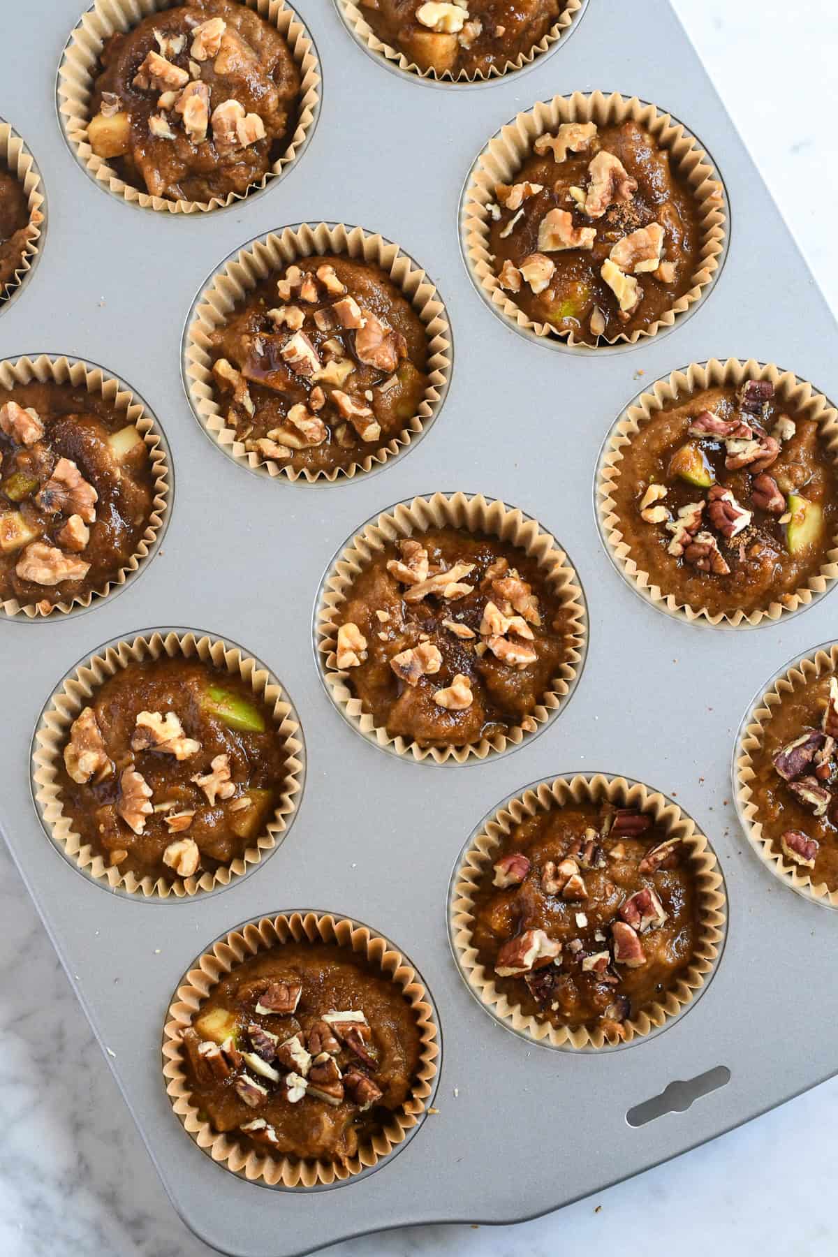 Healthy Apple Muffins raw batter in muffin tin topped iwth coconut sugar and walnuts