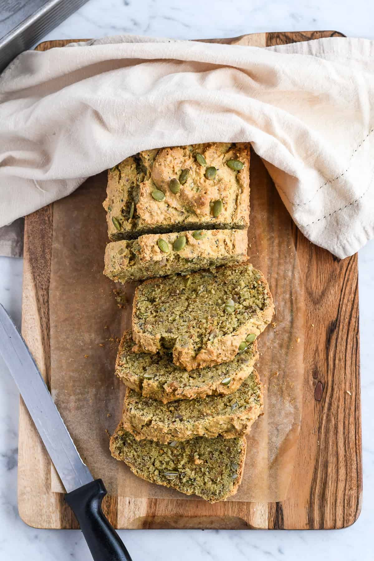 Easy Paleo Seed Bread (Gluten Free) slices on a board with napkin on part of the loaf and knife on side