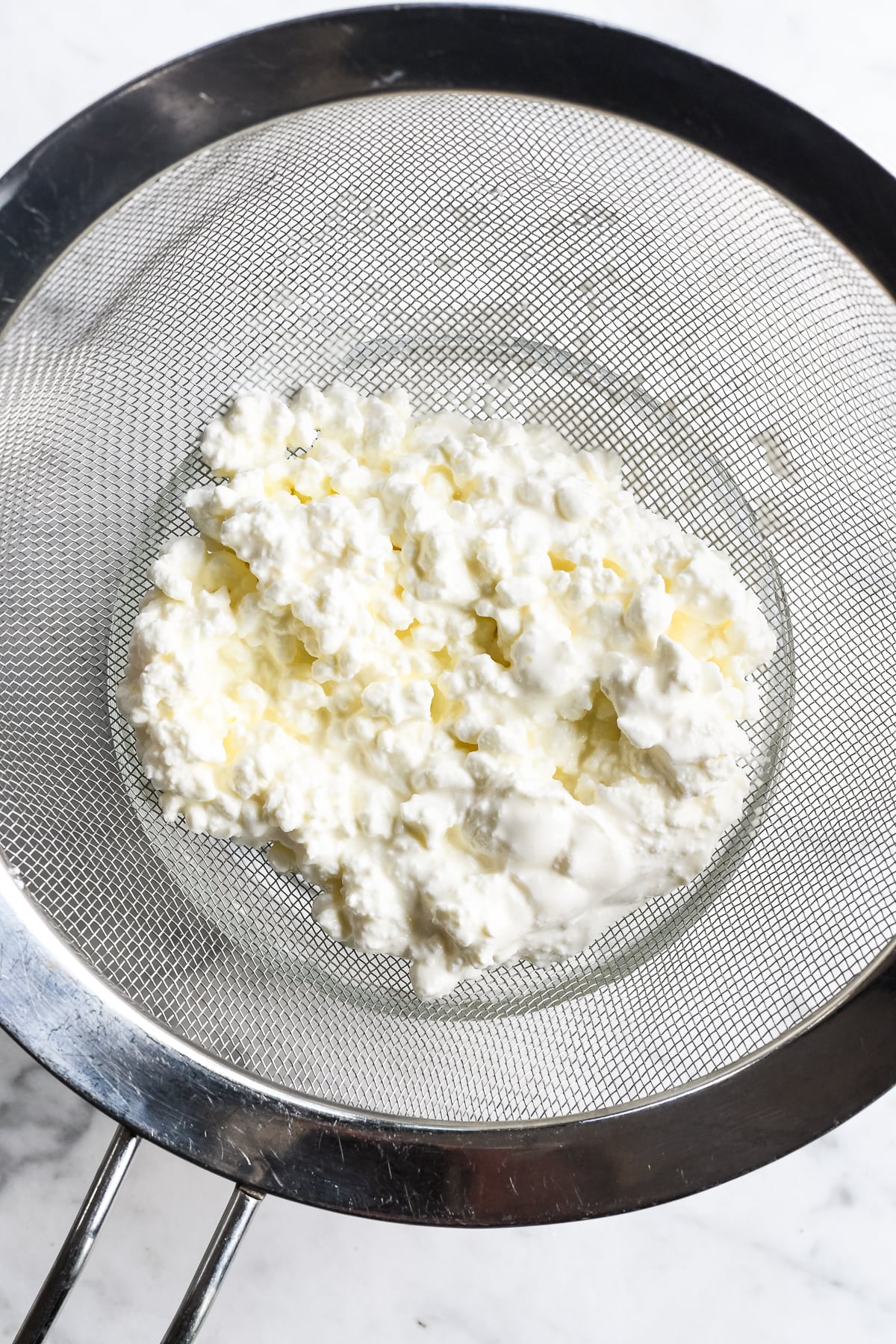 Easy Blueberry Cottage Cheese Bites draining the cottage cheese in a straine