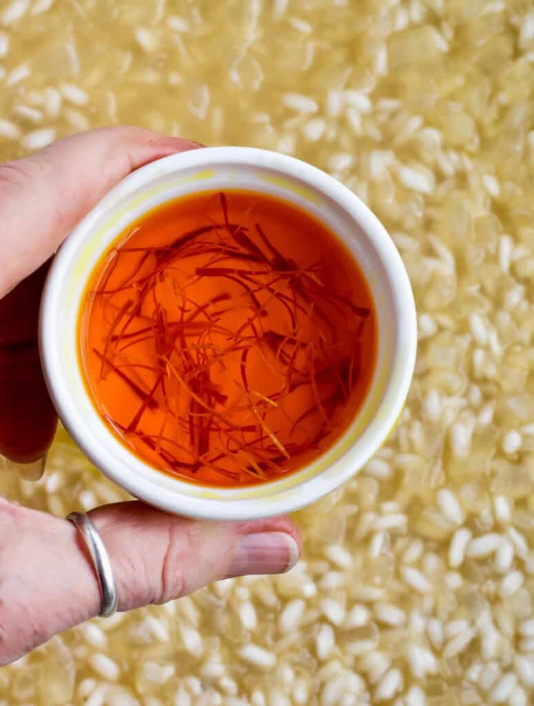 Saffron Risotto with Peas adding the bowl of saffron soaked in stock