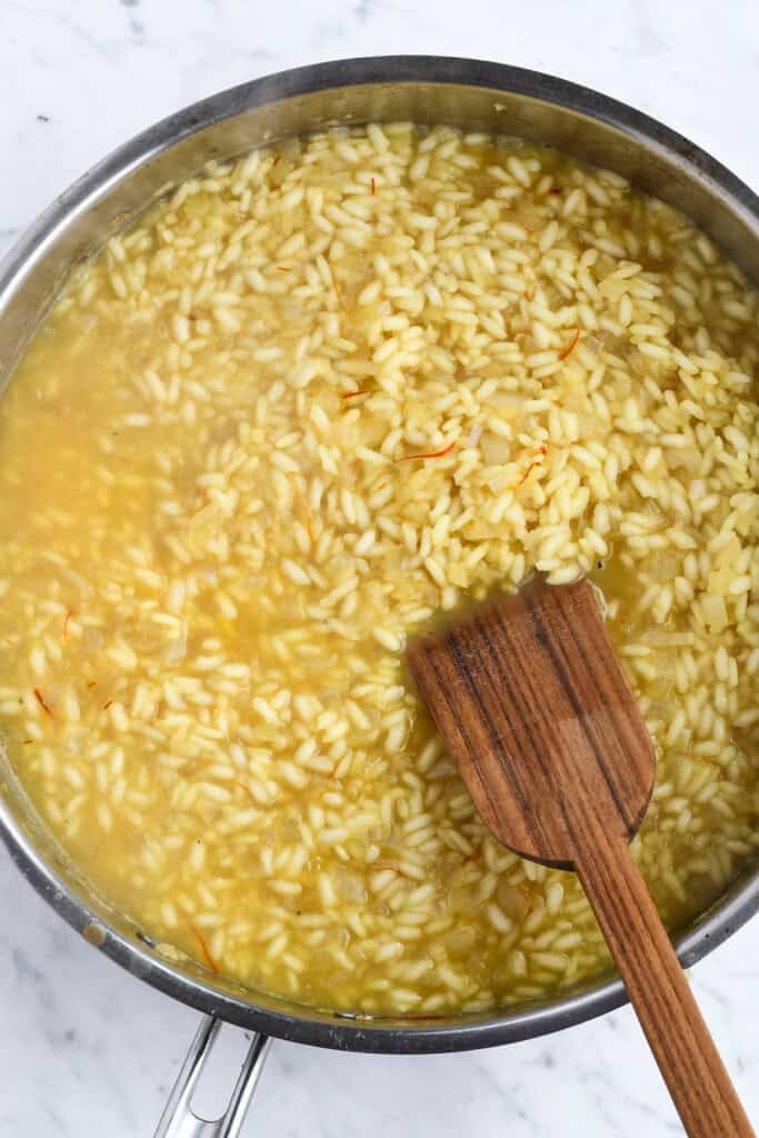 Saffron Risotto with Peas in pan with stock and wooden spoon