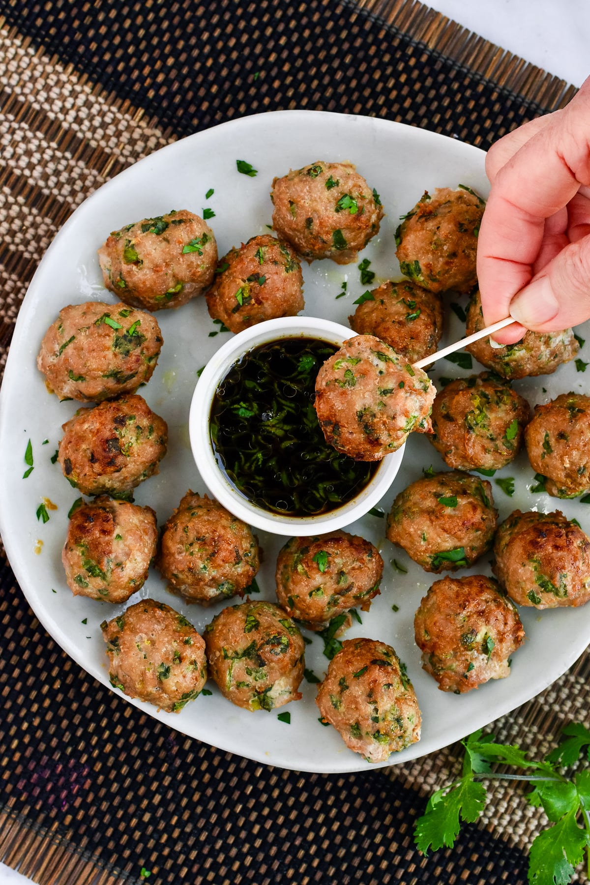 Easy Asian Turkey Meatballs on a platter with Asian Dipping Sauce and a hand holding a meatball and dipping