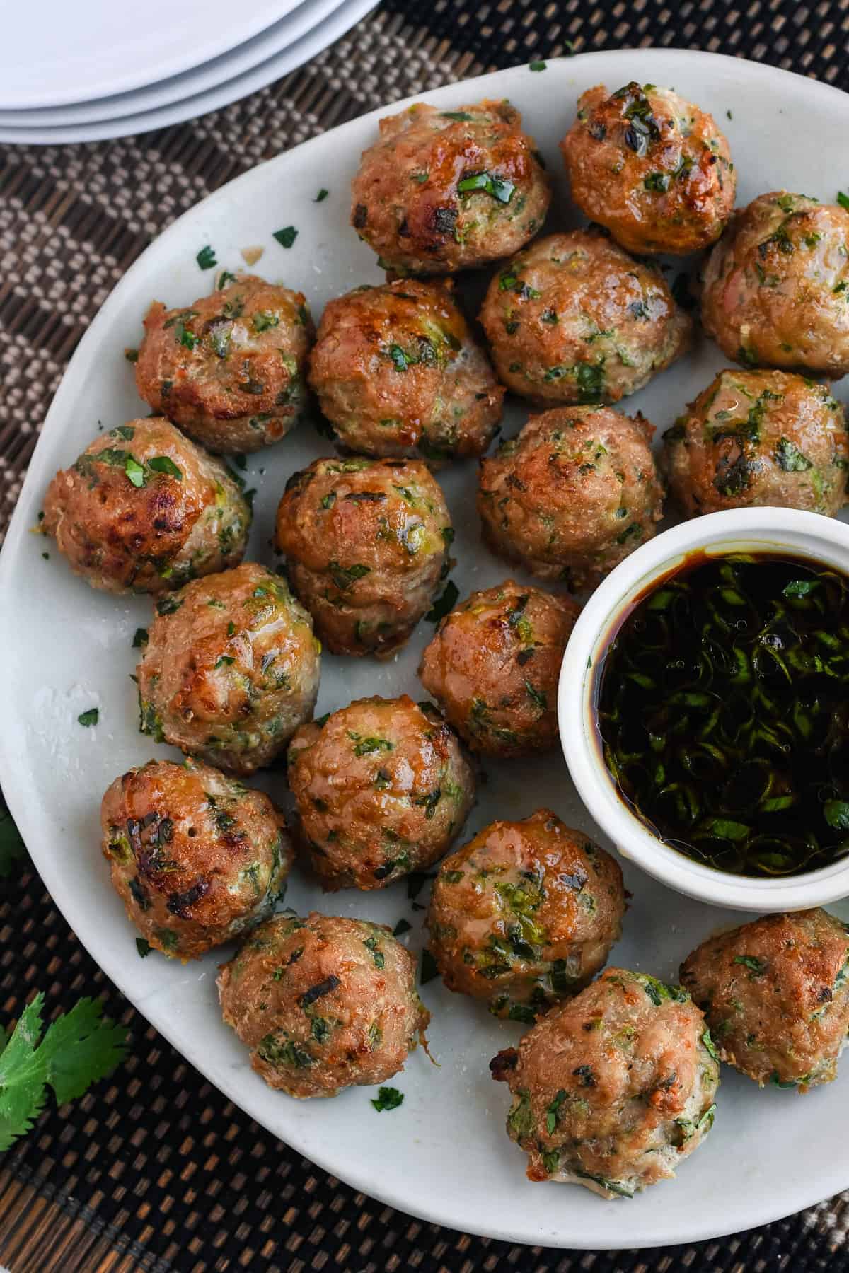 Asian Turkey Meatballs on a platter with dipping sauce and 3 plates on the side