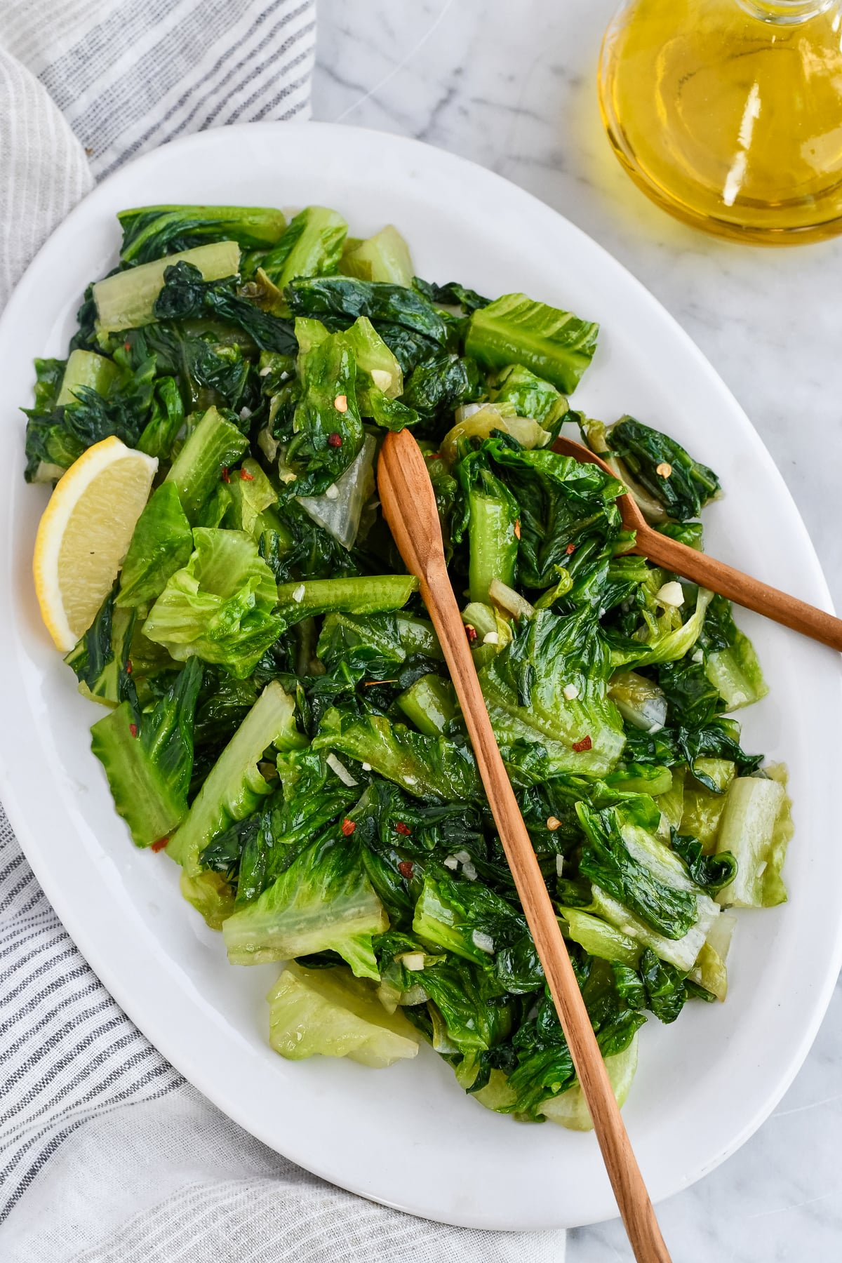 Easy Sautéed Romaine on platter with wooden serving spoons and lemon wedge