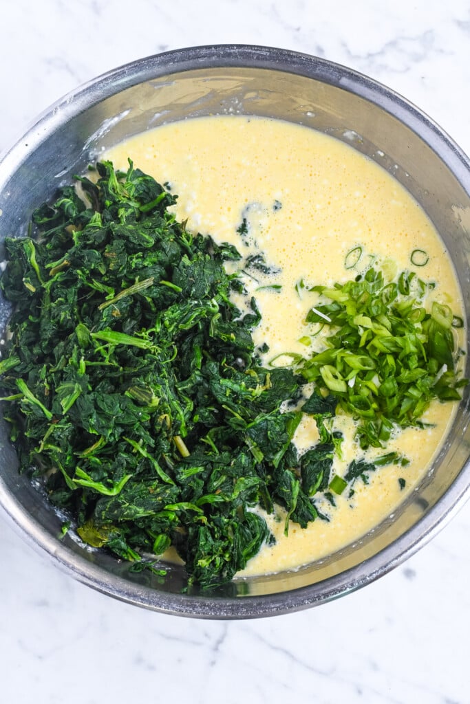 High Protein Spinach Egg Bites egg and cottage cheese mixed with spinach and scallion on top being added